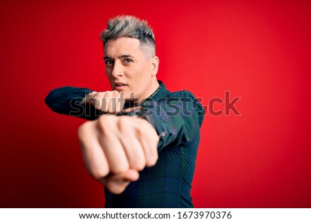 Young handsome modern man wearing elegant green shirt over red isolated background Punching fist to fight, aggressive and angry attack, threat and violence