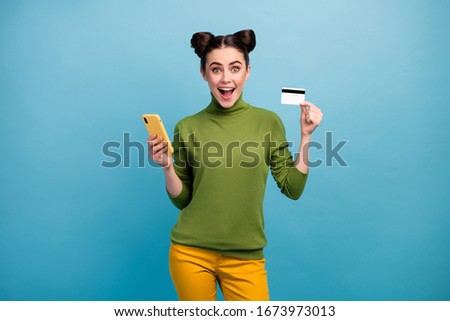 Photo of attractive millennial lady hold telephone plastic credit card advising new service online payment wear green turtleneck yellow pants isolated blue color background