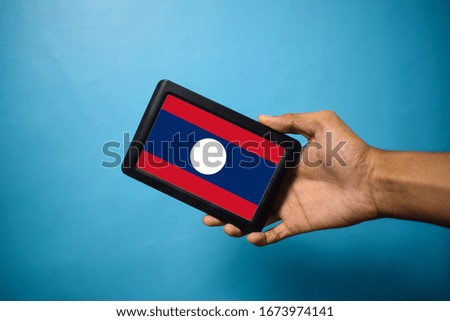 Man holding Smartphone with Flag of Laos.Laos Flag on Mobile Screen isolated On Blue Background