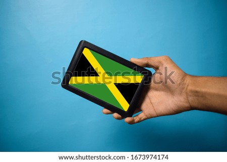 Man holding Smartphone with Flag of Jamaica. Jamaica Flag on Mobile Screen isolated On Blue Background
