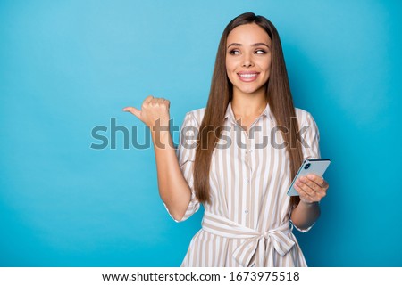 Sale. Photo of pretty attractive lady blogger hold telephone arms chatting friends directing thumb finger side empty space wear casual striped dress isolated blue color background