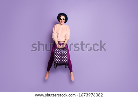 Full body photo of funny pretty lady jumping up high airport hold carry luggage youngster tourist wear cap sun glasses trendy pink pullover pants isolated purple color background