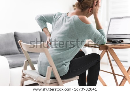 Woman working on a laptop and having headache and back, hip, spine pain. Royalty-Free Stock Photo #1673982841