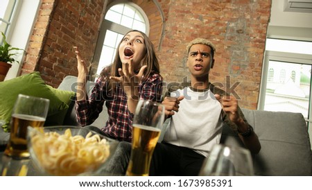 Emotional. Excited couple, friends watching sport match, chsmpionship at home. Multiethnic friends, fans cheering for favourite national basketball, tennis, soccer, hockey team. Concept of emotions.