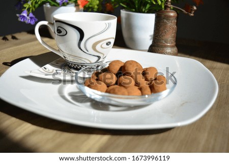 A coffee cup placed on a wooden table with some nuts and chocolate