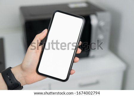 Hand holding blank screen of smartphone at home in kitchen. for graphic display montage.