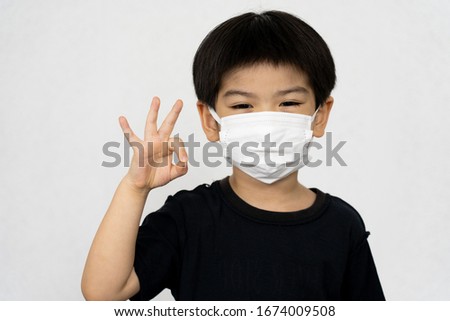 asian boy in black t-shirt posting "OK" sign waring protection mask from coronavirus and air pollution isolated on white background,Health care concept. Selective focus at the face of model.