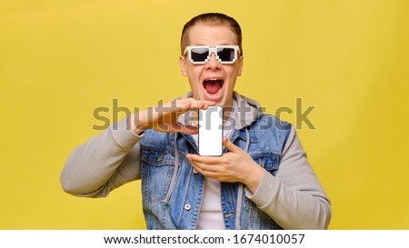 Stylish Caucasian man in a jeans on a yellow background with 8 bit glasses. Copy space. Close up. Holds smartphone with both hands.
