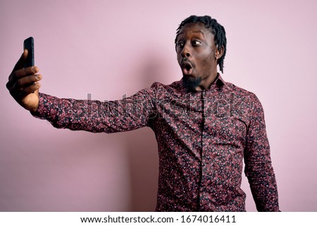 Young handsome african american man wearing casual shirt standing making selfie by camera scared in shock with a surprise face, afraid and excited with fear expression