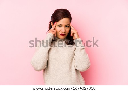 Middle age latin woman isolated on a pink background focused on a task, keeping forefingers pointing head.