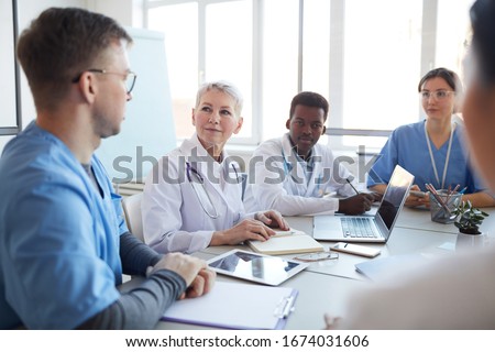 Portrait of mature female doctor heading committee meeting at medical council, copy space Royalty-Free Stock Photo #1674031606