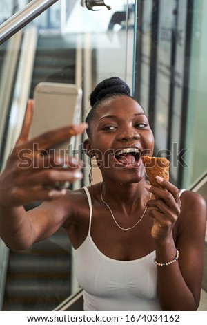 Young black woman taking a selfie from his phone while eating an ice-cream                             