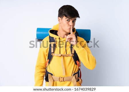 Young mountaineer man with a big backpack over isolated blue background doing silence gesture