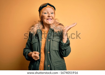 Senior beautiful grey-haired skier woman wearing snow sportswear and ski goggles smiling cheerful presenting and pointing with palm of hand looking at the camera.