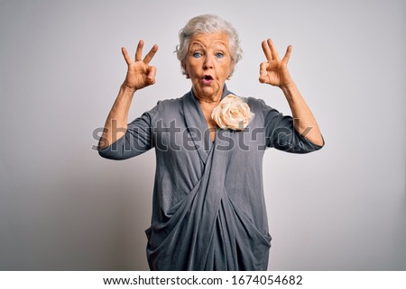 Senior beautiful grey-haired woman wearing casual dress standing over white background looking surprised and shocked doing ok approval symbol with fingers. Crazy expression