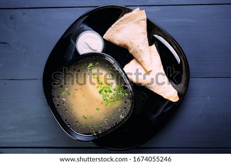 Fresh fish soup with egg in a black deep dish with pancakes and sour cream on a black background, top view. Blue wooden background