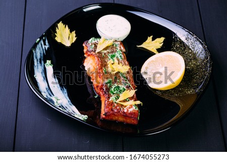 One piece of baked salmon grilled pepper, lemo and white souse on a black plate. wood blue background