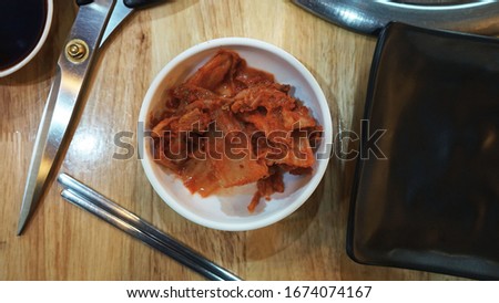 Pictures of kimchi, side dishes for Korean grilled restaurants Served with an appropriate amount on a white bowl In the illustration with grilling equipment such as plates, scissors