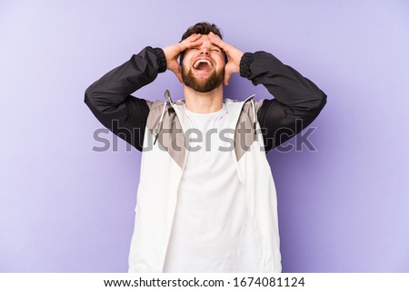 Young caucasian man isolated on purple background laughs joyfully keeping hands on head. Happiness concept.
