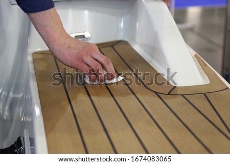 A man's hand rubs oil on marine teak on the deck of a white motor yacht , motor boat maintenance Royalty-Free Stock Photo #1674083065