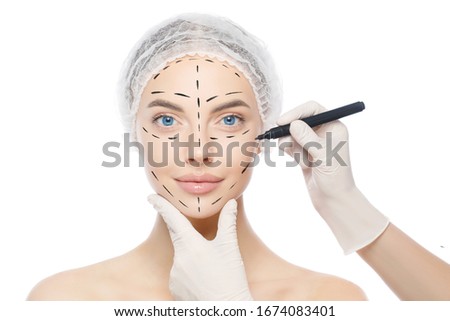Plastic surgery or face lifting for young woman. Doctor's hands wearing gloves drawing lines, holding head of female patient, isolated on white background Royalty-Free Stock Photo #1674083401