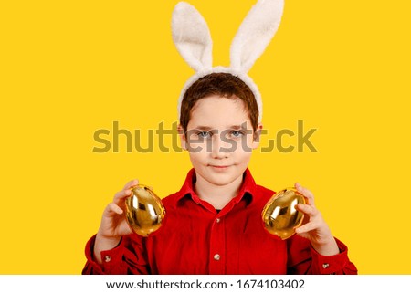 Cute boy in bunny ears headband holding Golden Easter eggs