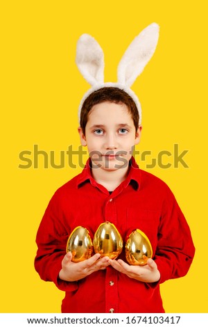 Attractive boy in bunny ears headband holding Golden Easter eggs