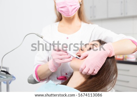 A woman dentist photographs the teeth of a patient using a special camera in a modern dental chair.