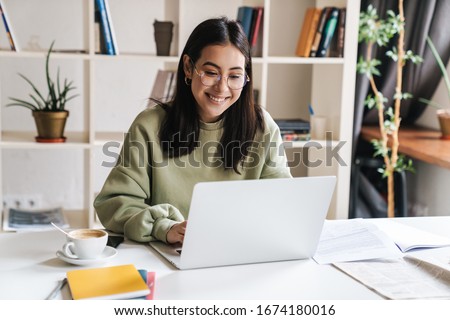 Attractive happy young girl student studying at the college library, sitting at the desk, using laptop computer Royalty-Free Stock Photo #1674180016