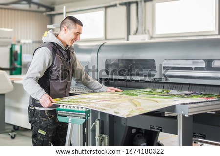 Technician worker operator works on large premium industrial printer and plotter machine in digital printshop office Royalty-Free Stock Photo #1674180322