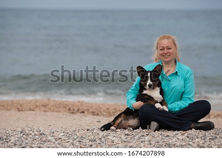 An adult woman with her dog Welsh Corgi cardigan sitting on the beach at the sea. copyspace. The concept of a warm relationship between the owner and the pet, traveling with a dog.