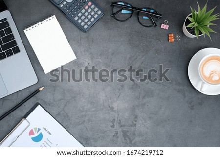 Flat lay business office concept on vintage cement table desk background with blank notepad and laptop computer, calculator and document, coffee cup and green plant, eye glasses, Top view, copy space