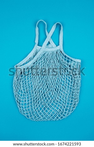 Top view of turquoise empty reusable string mesh eco bag for shopping  on blue background. Zero waste and plastic free concept. Sustainable lifestyle.
