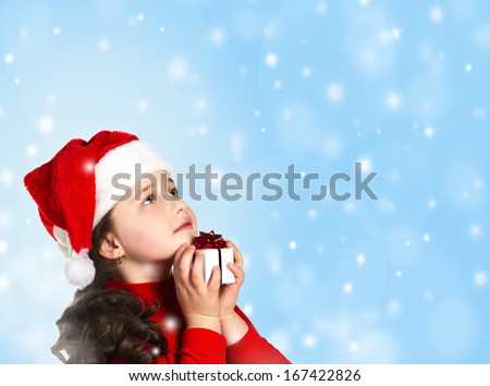 profile portrait of a little girl in santa hat and red cloth with present box looking up on blue sky and snow background