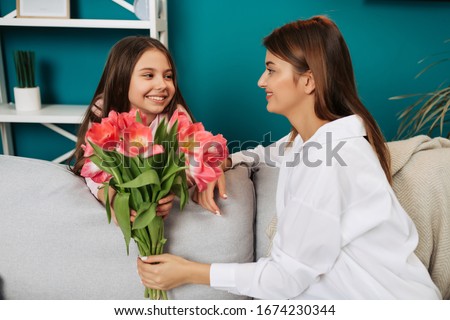 I love you, mom! Attractive young woman with little cute girl are sitting on bed and spending time together at home. Mom is receiving presents from daughter on Mother's Day. Happy family concept