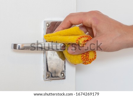 Man cleaning a door knob. Cleaning a silver handle with a yellow chiffon. Disinfecting to kill germs, viruses and bacteria Royalty-Free Stock Photo #1674269179