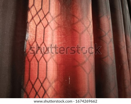 Classic red fabric curtain with sunlight in the background.