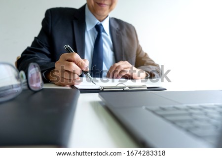 Businessman in the chairman position work on the table, hold the pen with the eyeglasses on the desk and paperwork.
 Royalty-Free Stock Photo #1674283318