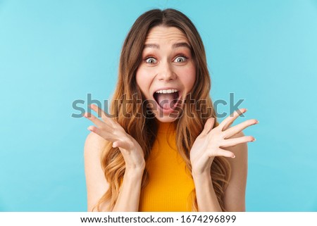 Portrait of a cheerful excited pretty young girl standing isolated over blue background, looking at camera