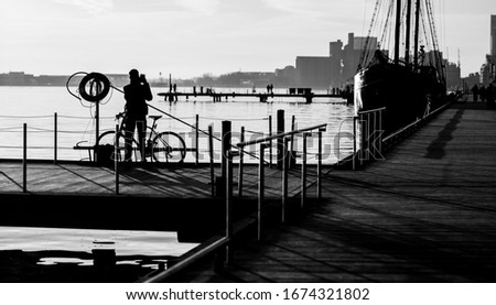 Black and white shot of a dock where there is a silhouette of person taking a photo next to their bike