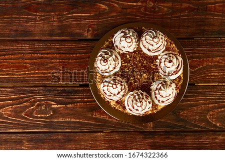 Roasting meringue cake with nuts and cream on wood background with copy space. Abstract  birthday cake with glazed caramel and meringue, close-up. Candied roasted cake