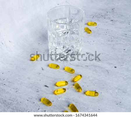 Medicine yellow capsules with glass of water on gray background.