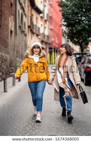 Stock photo of two young girls walking down the street having fun. They are holding hands and smiling.