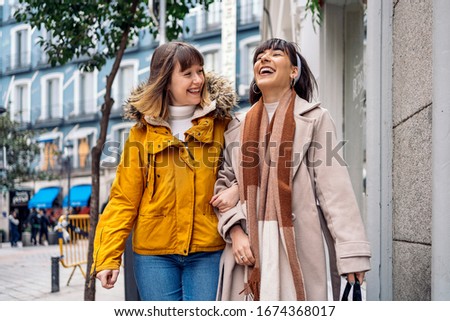 Stock photo of two young girls walking down the street having fun. They are holding arms and laughing.