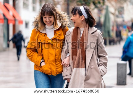 Stock photo of two young girls walking down the street having fun. They are holding arms and smiling.