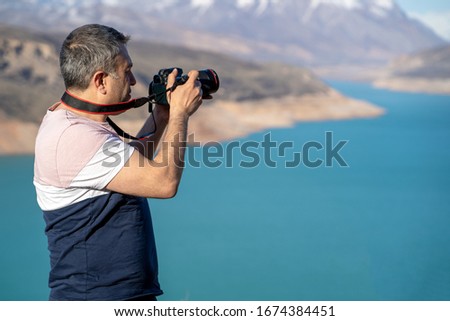Amateur photographer holding a camera in a mountain background.
