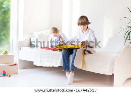 Happy brother and baby sister opening their presents on a sunny morning in a white bedroom with a big window