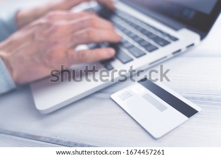 Online shopping concept. Man making online payment on laptop. Bank card on the table. Toned soft focus picture.