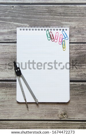 Notepad with a blank white sheet in a checker paper and with compass lies on the background of wooden boards.