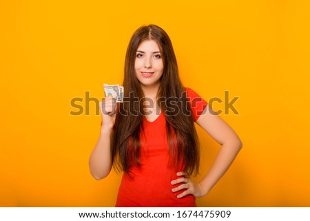 Attractive, young woman holds money notes in her hands, concept of savings and cashback. Studio photo on a yellow background.